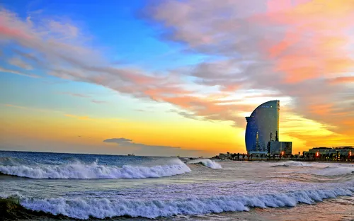 Sonnenuntergang am Strand mit großen Wellen und modernem Gebäude im Hintergrund.