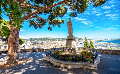 Statue im Park mit Blick auf Stadt und Meer unter blauem Himmel.