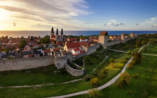 Luftaufnahme einer mittelalterlichen Stadt mit Stadtmauer, Kirche und Küstenlinie im Hintergrund.