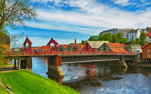 Rote Holzbrücke über Fluss mit bunten Häusern im Hintergrund.