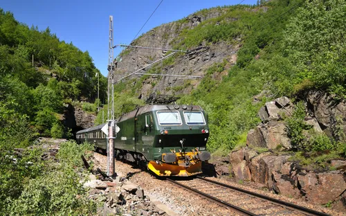 Flåmsbana, malerische Eisenbahn in Norwegen, fährt durch grüne Landschaft und Felswände.