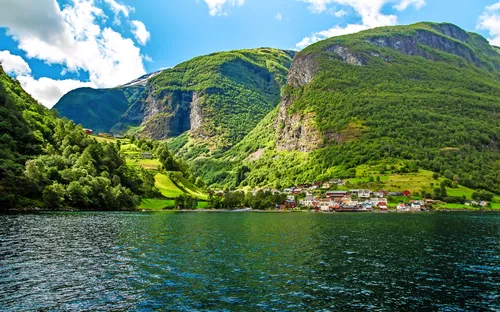 Küstenlandschaft mit Bergen und kleinem Dorf am Wasser.