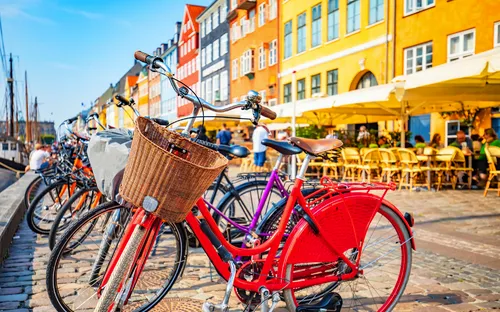 Fahrräder am Kai einer bunten, sonnigen Hafenstraße mit Café in der Nähe.