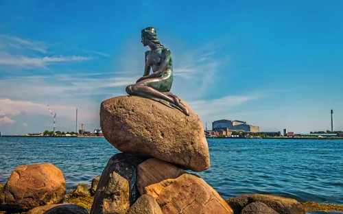 Eine Meerjungfrau-Statue sitzt auf einem Felsen am Wasser.