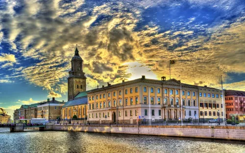 Historisches Gebäude an einem Fluss bei Sonnenuntergang mit dramatischem Himmel.