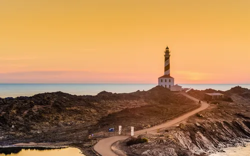 Leuchtturm bei Sonnenuntergang am Meer mit felsiger Landschaft