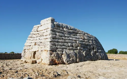 Steinpyramidenartiges Bauwerk auf einem trockenen, felsigen Gelände unter klarem blauem Himmel.