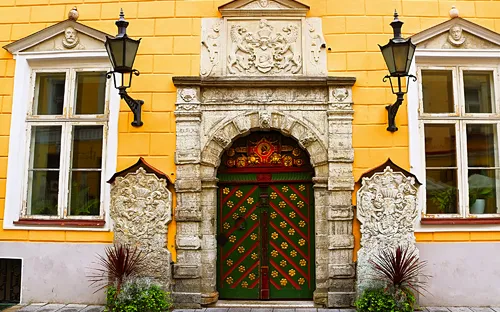 Ornate Eingangstür in gelber Fassade mit zwei Fenstern und Laternen.