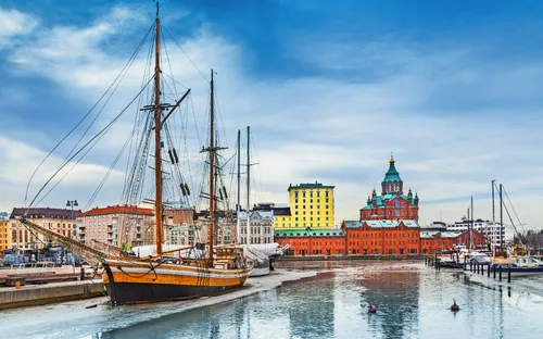Hafen mit Segelschiff und historischen Gebäuden bei klarem Himmel.