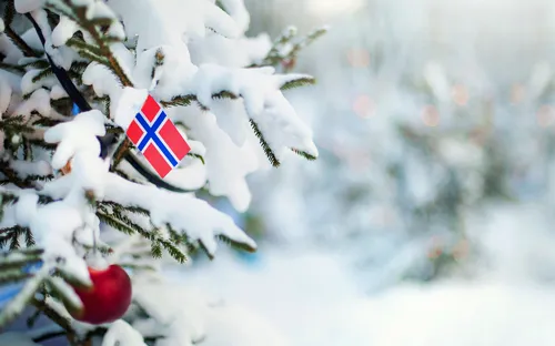 Verschneiter Weihnachtsbaum mit norwegischer Flagge und roten Kugeln.