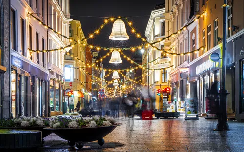 Beleuchtete, festlich geschmückte Straßenszene bei Nacht mit verschwommenen Spaziergängern.