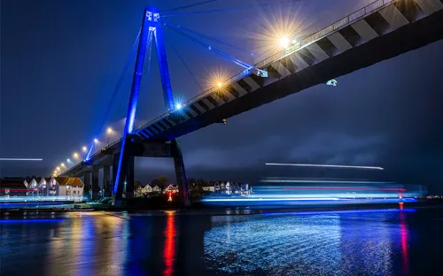Brücke bei Nacht mit Lichtspuren und beleuchteter Stadt im Hintergrund.